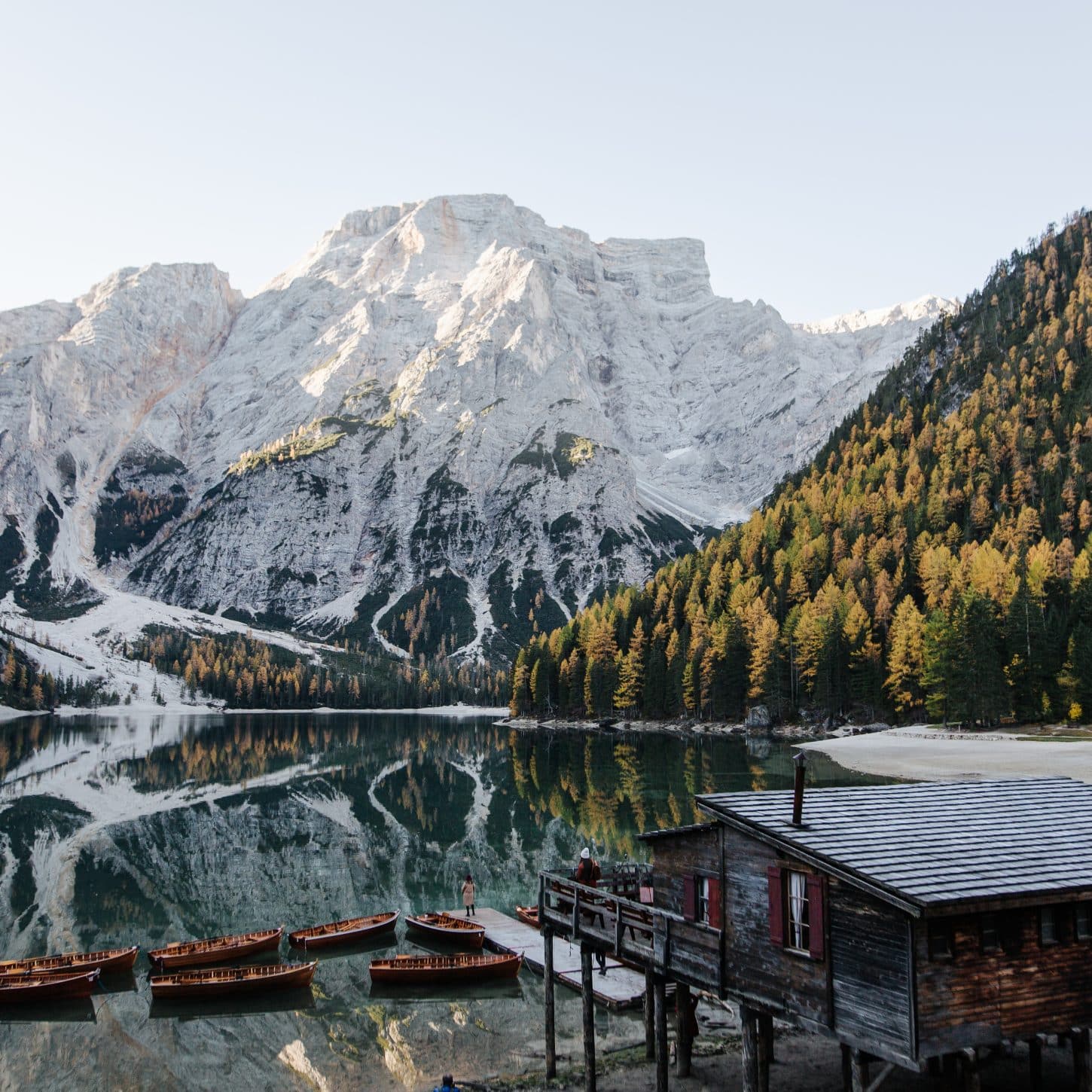 Wooden rowboats docked at a rustic boathouse on Lago di Braies with snow-capped Dolomite mountains reflecting in the calm alpine lake, Italy