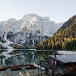Wooden rowboats docked at a rustic boathouse on Lago di Braies with snow-capped Dolomite mountains reflecting in the calm alpine lake, Italy