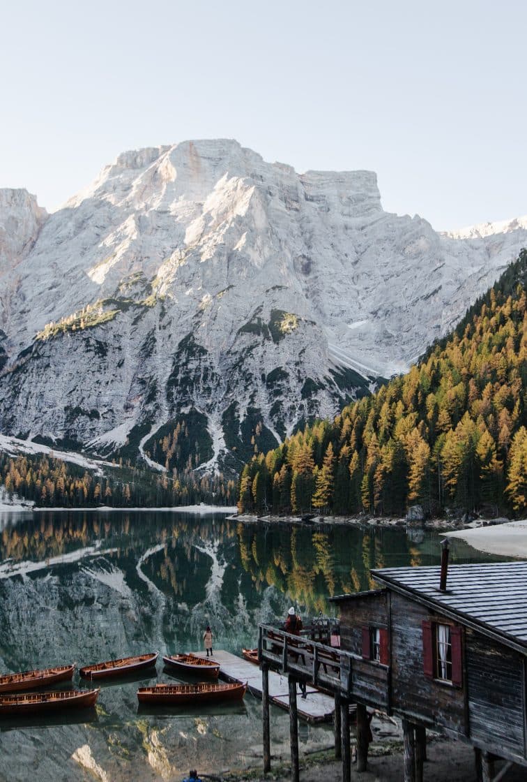 Wooden rowboats docked at a rustic boathouse on Lago di Braies with snow-capped Dolomite mountains reflecting in the calm alpine lake, Italy
